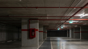 Garagem com sprinklers no teto, extintor sinalizado e saída de emergência iluminada